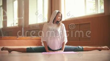 年轻漂亮的女人坐在瑜伽垫上做腿部伸展运动<strong>舞蹈工作室</strong>