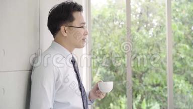慢动作-成熟的亚洲商人喝着咖啡，从办公楼向窗外<strong>眺望城市</strong>的天际线