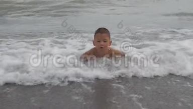 孩子躺在海浪中的沙岸上。 男孩在海滩上划沙。 孩子洗了海浪。