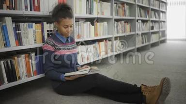 年轻的非裔美国妇女正坐在大学图书馆的地板上看书。