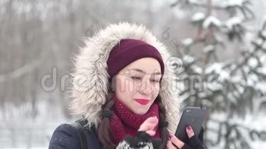 美丽的年轻<strong>女孩</strong>在冬天的公园里散步时，正在智能手机上浏览<strong>社交网络</strong>。