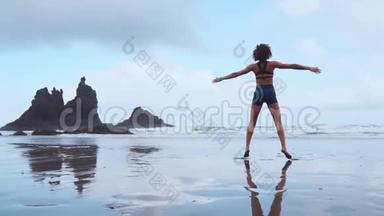 女孩在大西洋附近的黑沙滩上跳汉堡包，背景是群山