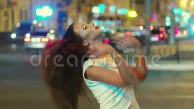 夜城的一个微笑的女孩在玩她的棕色长发，背景是城市交通