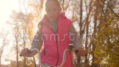 女孩的手拿着弯曲的自行<strong>车把手</strong>。 女孩骑自行<strong>车</strong>，在秋天的公园里微笑。 特写