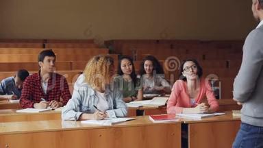 漂亮的年轻女子勤奋的学生和坐在课桌前的高中老师交谈，而其他学生则微笑着