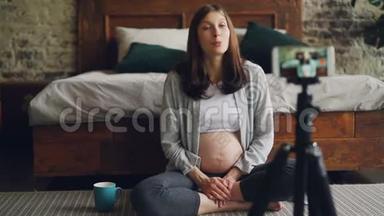 美丽的孕妇著名博主正在为关注智能手机摄像头和坐着聊天的人录制视频