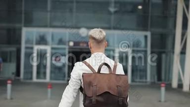 在工作的商人。 英俊的年轻人穿着白色衬衫，背着背包跑到机场，看着钟。 旅费