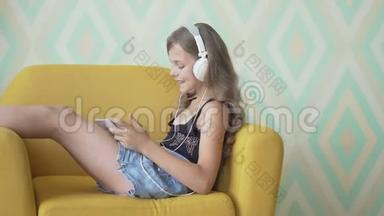 戴着耳机的漂亮<strong>小女孩</strong>在家里坐在沙发上用平板电脑<strong>听音乐</strong>