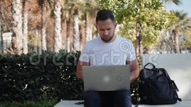微笑的年轻人在笔记本电脑上工作，坐在长凳上，拿着<strong>旅行箱</strong>和包，背包游客在度假
