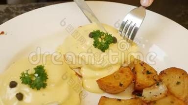 女人拿着刀叉吃鸡蛋本尼迪克特。 鸡蛋本尼迪克特面包，番茄和乡村烤土豆