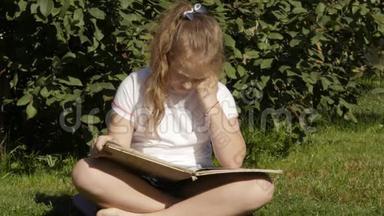 美丽的少女坐在夏天公园的草地上看书。 慢动作