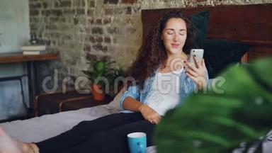 快乐的女孩在网上聊天，用智能手机看手机摄像头，用微笑坐在卧室的床上
