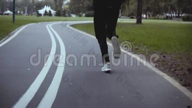 人沿着弯弯曲曲的公园路奔跑.. 后景。 慢动作。 穿白色运动鞋的运动员在安静的小巷里慢跑。