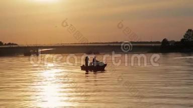 日落时分湖中一艘船上有钓竿的两名渔民的剪影