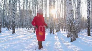 穿着红色冬季夹克和毛毡靴的可爱的年轻女子从寒冷中跳下来，并试图在带有桦树的图案城市公园保暖