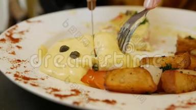 女人拿着刀叉吃鸡蛋本尼迪克特。 鸡蛋本尼迪克特面包，番茄和乡村烤土豆