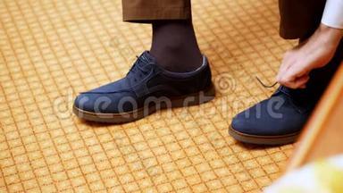 近距离看，男人的手系鞋带。这名男子正穿上他时髦的蓝色绒<strong>面皮</strong>鞋，背景是地毯。新郎