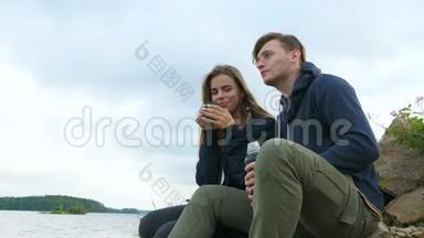 一个男人和一个女孩坐在河岸上<strong>喝热水</strong>瓶里的茶。