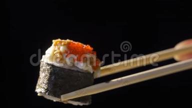 女孩拿筷子寿司在黑色镜面上，特写。 在黑暗中用筷子特写寿司卷