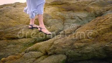 特写镜头。 女人穿着凉<strong>鞋</strong>`腿和一条长长的灰色裙子在低<strong>潮</strong>的岩石海岸上。