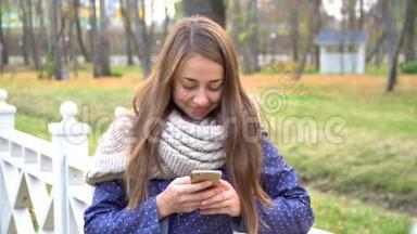 白人妇女戴着针织围巾，使用智能手机，在秋天公园散步时<strong>打字</strong>。 <strong>视频</strong>4k