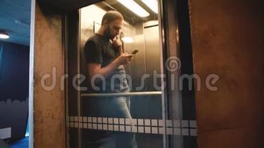 年轻快乐的休闲男子<strong>乘坐</strong>透明玻璃<strong>电梯</strong>，门打开，他走出使用智能手机购物应用程序。