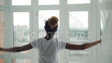 年轻的非洲裔美国女孩正走<strong>到家</strong>中的窗户前，拉开窗帘，然后从窗户欣赏风景