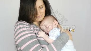 年轻美丽的黑发长发母亲，两个月大的新生儿睡在她的怀里。 妈妈抱着她
