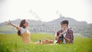 一对年轻夫妇穿着鲜艳的衣服坐在明亮的绿色草地上-一个男人弹吉他，而他的幸福<strong>女友</strong>