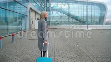 金发女孩<strong>在机场</strong>航站楼附近滚动一个手提箱-从后面看。 慢动作