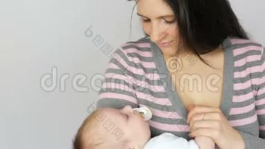 年轻美丽的黑发长发母亲，两个月大的新生儿睡在她的怀里。 妈妈抱着她