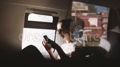 令人惊叹的反射镜头快乐的欧洲女孩微笑，使用智能手机应用程序坐在现代移动<strong>火车</strong>窗口<strong>座位</strong>。