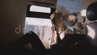 美丽快乐的白种人女孩微笑，在现代火车窗口座位上旅行时，在电话和挂断电话。