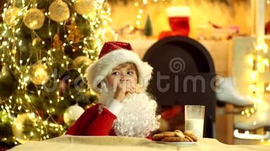 圣诞老人小孩在家里摘饼干和一杯牛奶。 圣诞老人-有趣的孩子采摘饼干。 吃圣诞小孩