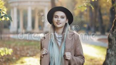 神奇的女孩穿着外套，戴着黑色帽子站在公园的小巷里，看着镜头，露出了惊人的微笑。 公园