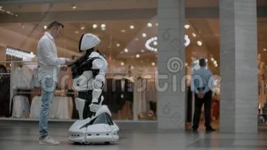 购物中心的那个人和一个机器人顾问沟通。 现代商店和机器人销售商。 机器人帮助一个男人
