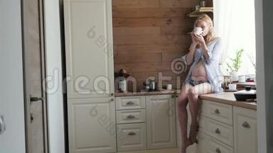 迷人的孕妇在厨房喝茶。孕妇坐在桌子上喝茶。