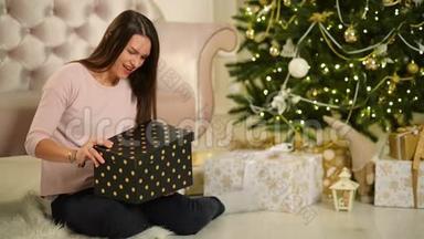 美丽的幸福女人坐在圣诞树旁边，手里拿着礼物。 圣诞快乐，新年理念。