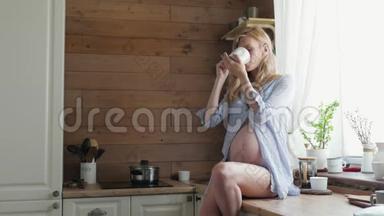 迷人的孕妇在厨房<strong>喝茶</strong>。孕妇坐在桌子上<strong>喝茶</strong>。