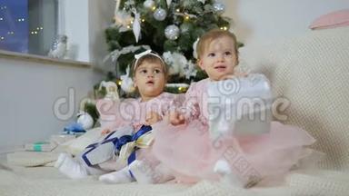 新年，穿着粉红色连衣裙的小姐姐们坐在格子布上，在圣诞树的背景下，放着礼品盒