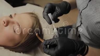 一个非常漂亮的女孩在美容院做一个层叠睫毛。 美容师把胶水涂在睫毛上。