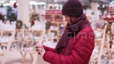 一个年轻漂亮的女人在圣诞商店，使用智能手机。 女人在商店里<strong>走来走</strong>去挑选圣诞装饰品