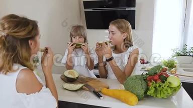 两个可爱的青少年姐妹和一个穿着白色衣服的妈妈在家里的厨房桌子上吃熟瓜。 健康食品、饮食