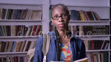 年轻漂亮的非洲裔<strong>美国</strong>妇女，戴眼镜，在<strong>图书馆</strong>看书，看相机，严肃而集中