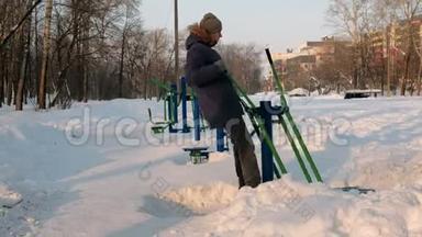 穿着带罩的蓝<strong>羽绒服</strong>的人在一个冬季城市公园里从事滑雪模拟器。 侧视。
