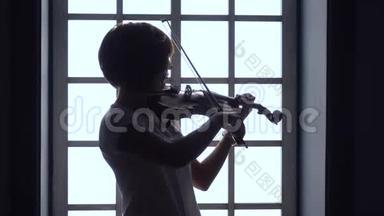 在窗户女孩拉小提琴的背景下。 剪影