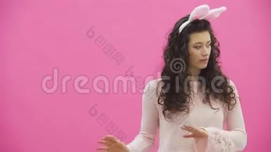 美丽的年轻<strong>女孩</strong>站在粉红色的背景上。 在这期间，头上有<strong>兔子</strong>的耳朵。 表演<strong>兔子</strong>