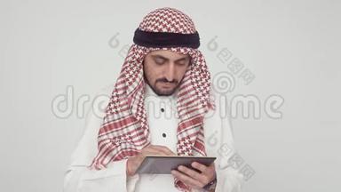 办公室里的现代阿拉伯人。 一个穿着国服的男人微笑着在数字平板电脑上打印。 在阿拉伯人手中的红色