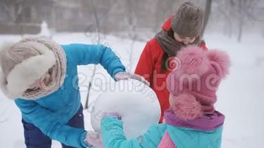 妈妈和两个女儿一起塑造了雪人。 户外冬季家庭游戏。