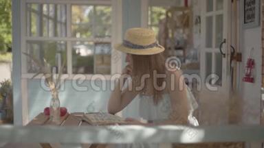 年轻的<strong>农</strong>村女孩戴着草帽和白色连衣裙，坐在户外的小木桌上看书。 <strong>农</strong>村